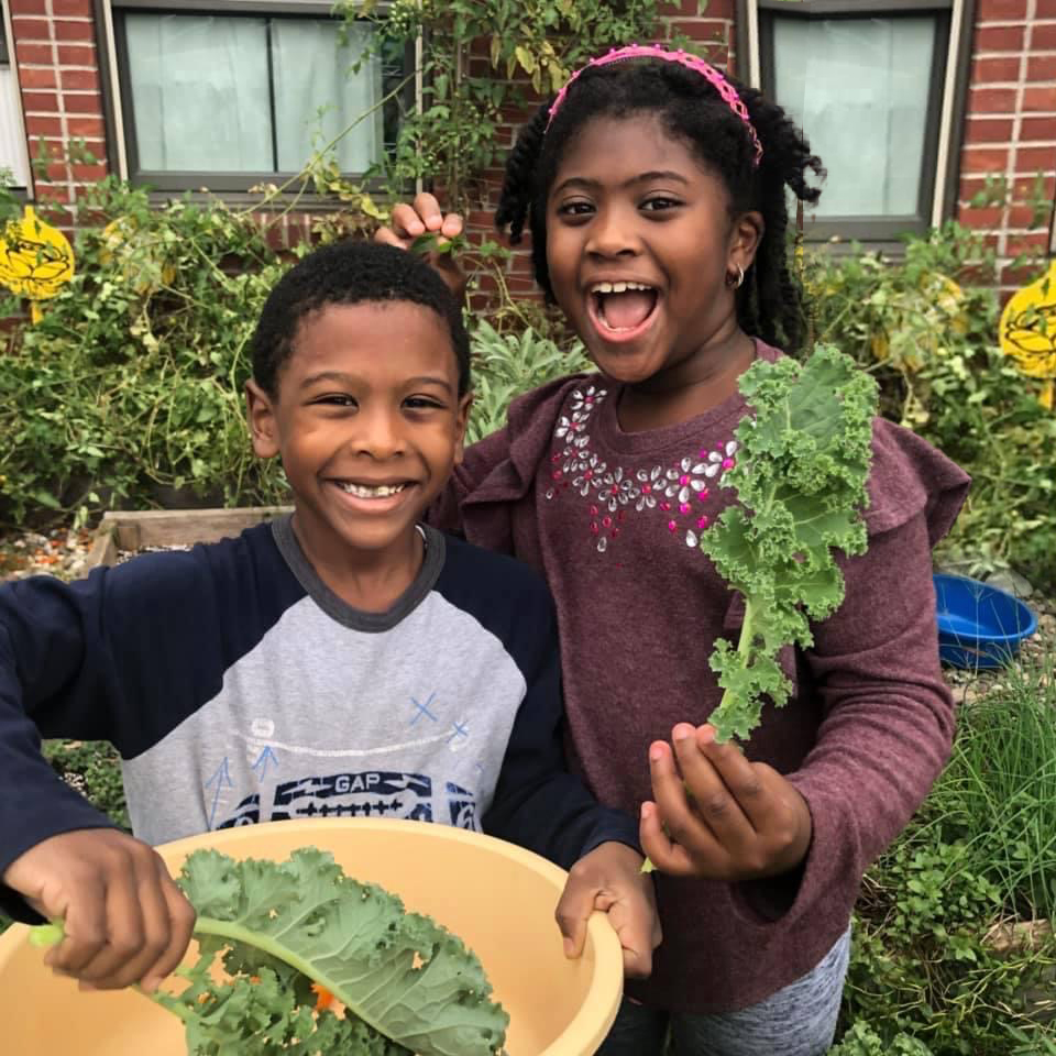 two young kids holding vegetables smiling
