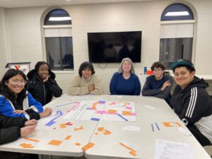Youth from the YMCA Farm Project and NoVo in Kingston staff play a handmade board game designed by the youth to help visualize and debate the interior floor plan of The Metro building